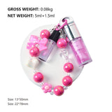 Two-piece Set Of Color-changing Lip Oils And A Bow-shaped Pearl Bracelet Charm.